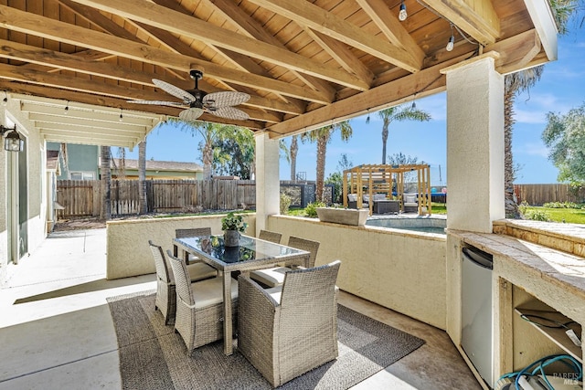 view of patio with exterior kitchen, outdoor dining space, a fenced backyard, and a ceiling fan