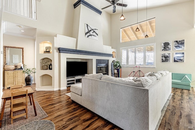 living room featuring a high ceiling, dark wood-type flooring, a ceiling fan, and a glass covered fireplace