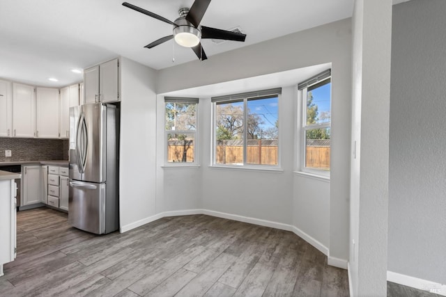 kitchen featuring tasteful backsplash, stainless steel fridge with ice dispenser, a ceiling fan, wood finished floors, and baseboards