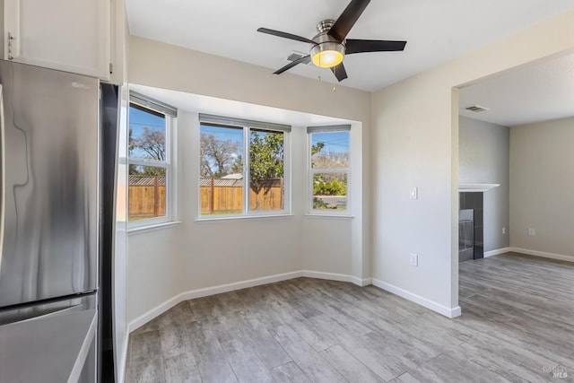 unfurnished room featuring light wood-style floors, baseboards, visible vents, and a ceiling fan