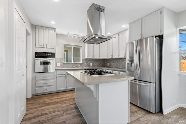 kitchen with island range hood, decorative backsplash, stainless steel appliances, light countertops, and a sink