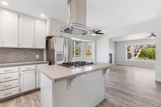 kitchen featuring stainless steel appliances, island exhaust hood, backsplash, and a ceiling fan