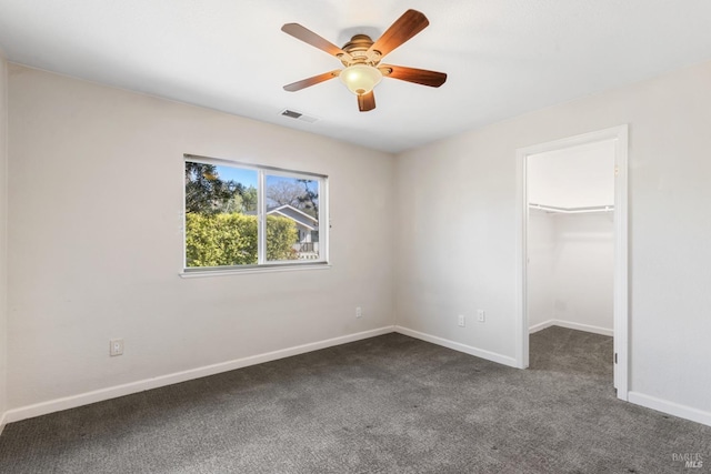 unfurnished bedroom with a walk in closet, baseboards, visible vents, and dark carpet