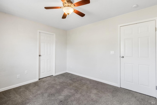 empty room featuring a ceiling fan, dark colored carpet, and baseboards