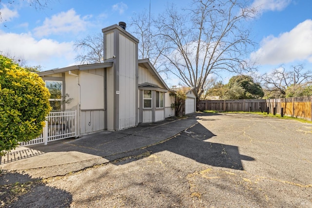 view of property exterior featuring a garage, a chimney, fence, and driveway