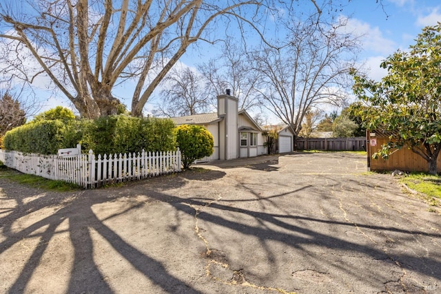 view of home's exterior featuring a fenced front yard, driveway, a chimney, and an attached garage