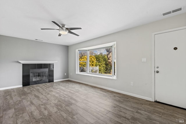 unfurnished living room with a fireplace, wood finished floors, visible vents, and baseboards