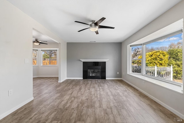 unfurnished living room featuring a fireplace, wood finished floors, a ceiling fan, and baseboards