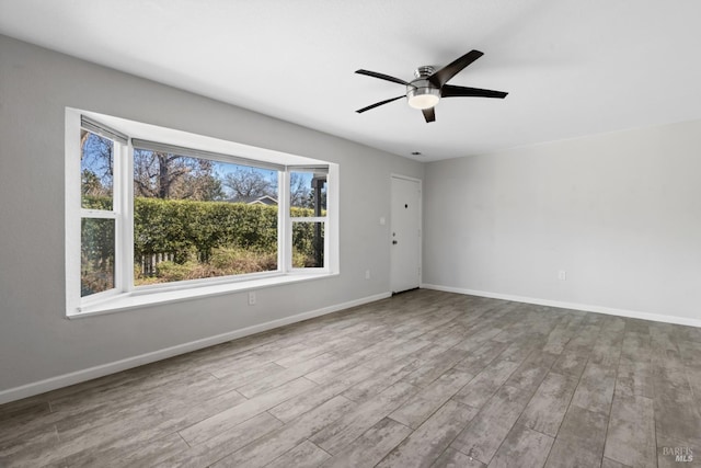 spare room with wood finished floors, a ceiling fan, and baseboards