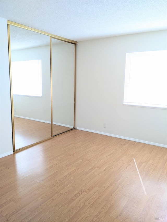 unfurnished bedroom featuring a closet, a textured ceiling, baseboards, and wood finished floors