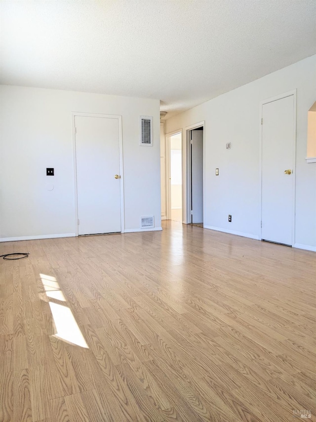 unfurnished room featuring light wood-type flooring, baseboards, visible vents, and a textured ceiling