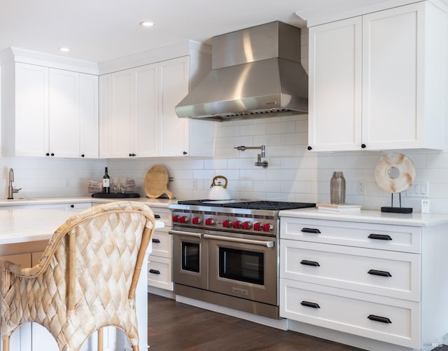 kitchen with light countertops, wall chimney range hood, range with two ovens, and dark wood finished floors