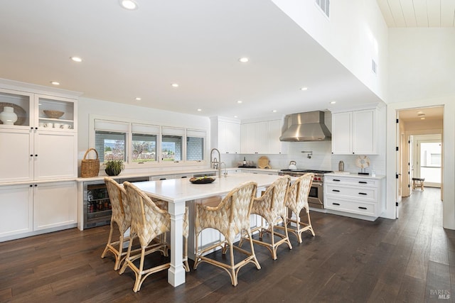 kitchen with wall chimney exhaust hood, a kitchen island with sink, stainless steel range, and a breakfast bar area