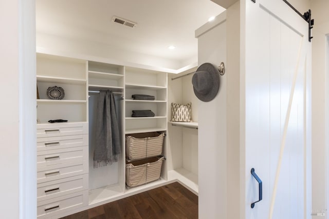 walk in closet featuring a barn door, dark wood finished floors, and visible vents