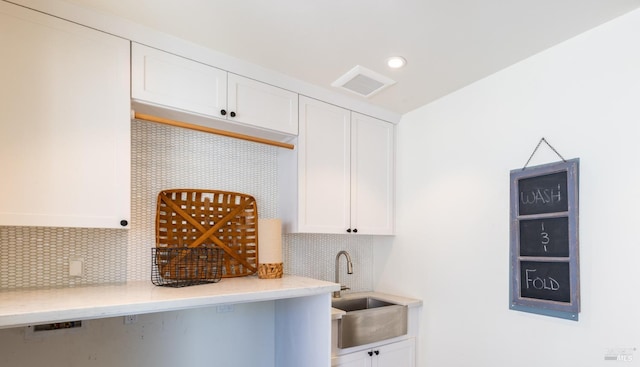 kitchen with decorative backsplash, a sink, visible vents, and white cabinets