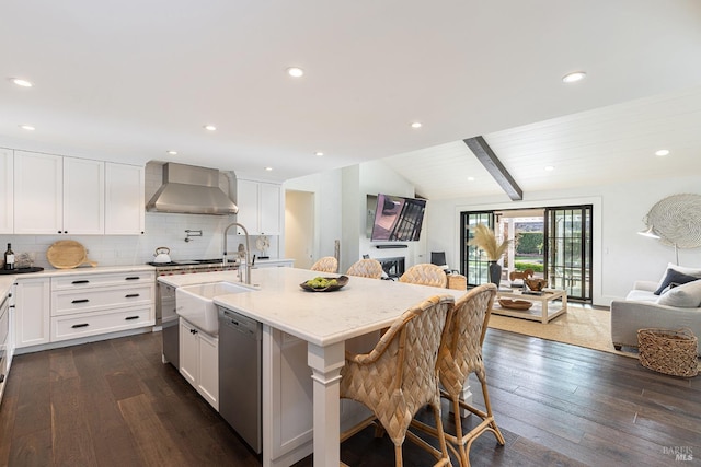 kitchen featuring dark wood-style flooring, backsplash, stainless steel dishwasher, open floor plan, and wall chimney range hood