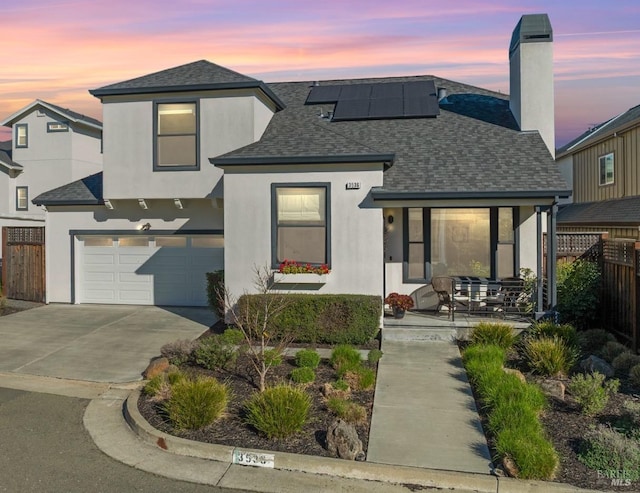 view of front facade featuring stucco siding, a shingled roof, concrete driveway, roof mounted solar panels, and fence