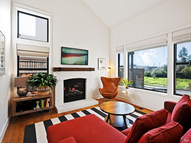 living room with high vaulted ceiling, a brick fireplace, wood finished floors, and baseboards