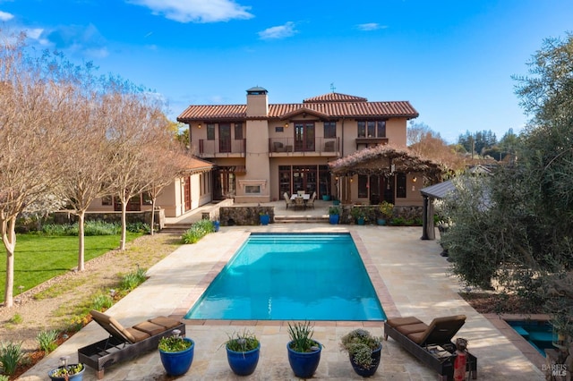 rear view of house with stucco siding, an outdoor pool, a balcony, a chimney, and a patio area