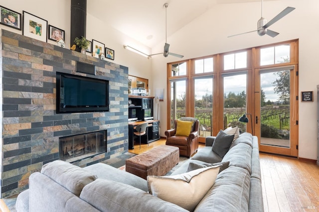 living area with light wood-type flooring, high vaulted ceiling, a glass covered fireplace, and a ceiling fan