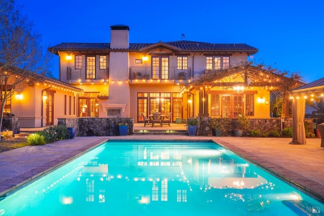 rear view of house with a balcony, an outdoor pool, stucco siding, a chimney, and a patio area