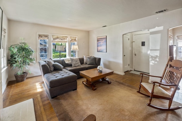 living area with baseboards, arched walkways, wood finished floors, and visible vents
