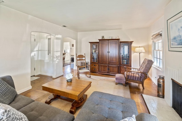 living area with arched walkways, baseboards, and light wood-type flooring
