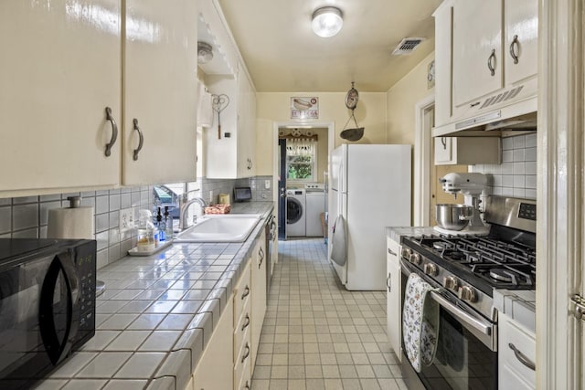 kitchen with visible vents, black microwave, stainless steel gas stove, tile counters, and under cabinet range hood