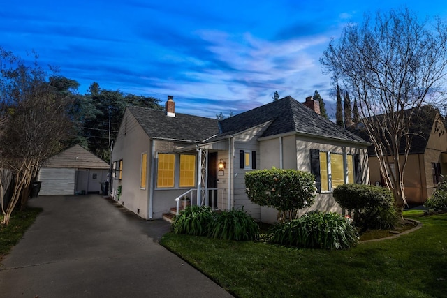 bungalow-style house featuring an outdoor structure, stucco siding, a chimney, a lawn, and a detached garage