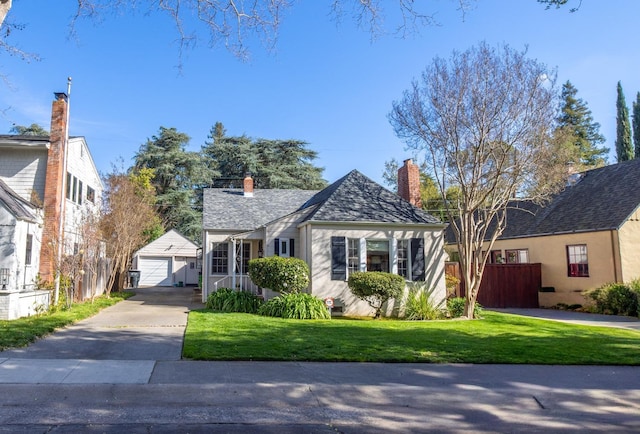 bungalow-style house with a chimney, a front yard, a garage, an outdoor structure, and concrete driveway