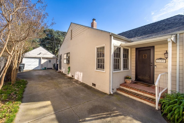 exterior space with crawl space, driveway, a chimney, a detached garage, and an outdoor structure