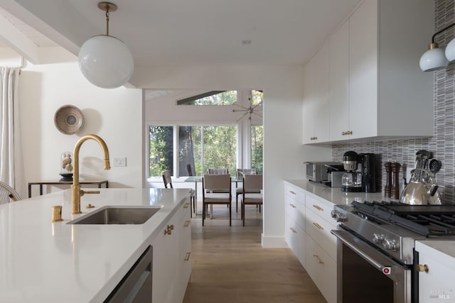 kitchen featuring light countertops, light wood-style flooring, decorative backsplash, a sink, and high end range