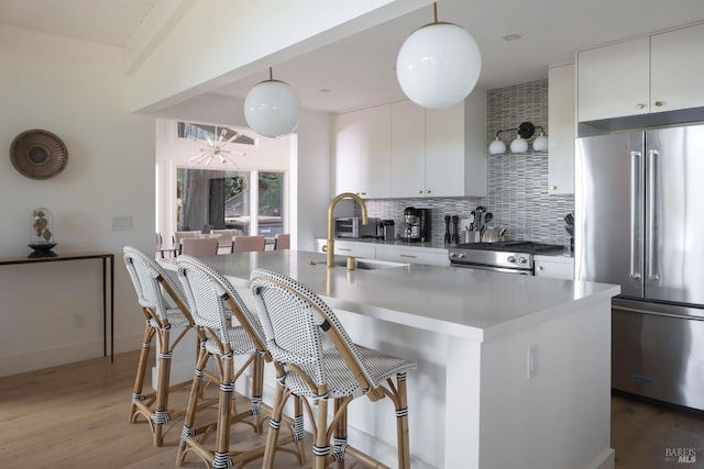 kitchen featuring tasteful backsplash, white cabinets, decorative light fixtures, stainless steel appliances, and a sink