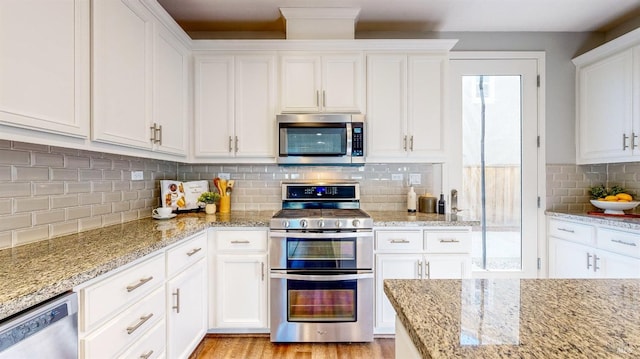 kitchen with stainless steel appliances, decorative backsplash, light stone countertops, and white cabinets