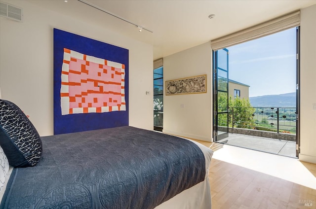 bedroom with access to exterior, visible vents, floor to ceiling windows, rail lighting, and wood finished floors