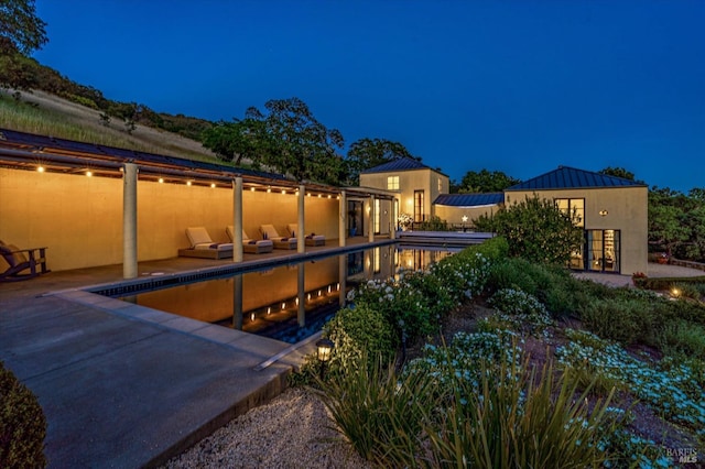 pool at twilight with an outdoor pool and a patio area