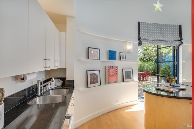 kitchen with light wood finished floors, dark stone countertops, white cabinets, and a sink