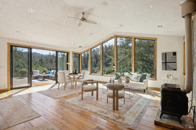 sunroom featuring vaulted ceiling, ceiling fan, and a wood stove