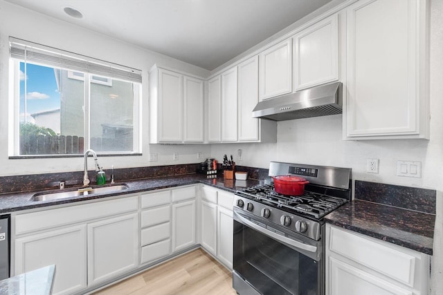 kitchen with stainless steel range with gas cooktop, white cabinets, a sink, dark stone counters, and under cabinet range hood