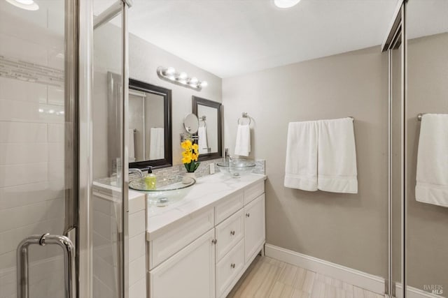 full bathroom featuring a stall shower, a sink, baseboards, and double vanity