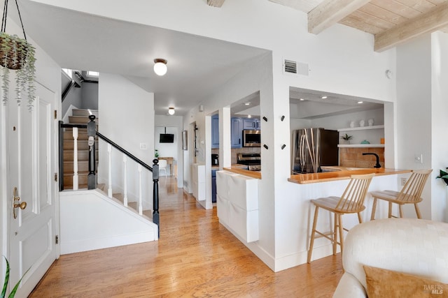 kitchen featuring light wood finished floors, visible vents, a breakfast bar area, stainless steel appliances, and beam ceiling