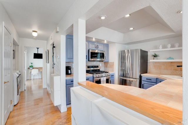 kitchen with a raised ceiling, light wood-style floors, appliances with stainless steel finishes, blue cabinetry, and open shelves