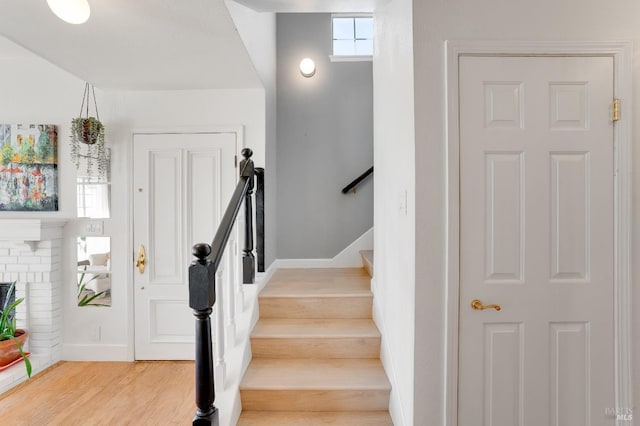 stairway with a brick fireplace, wood finished floors, and baseboards