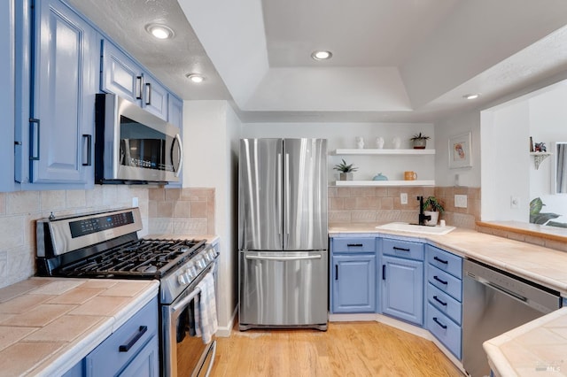 kitchen with tile countertops, blue cabinetry, light wood-type flooring, and appliances with stainless steel finishes