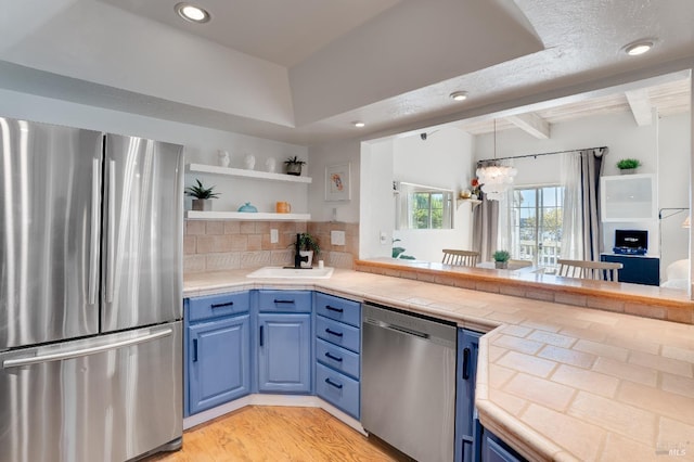 kitchen with appliances with stainless steel finishes, blue cabinetry, open shelves, tasteful backsplash, and beamed ceiling