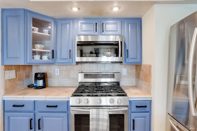 kitchen featuring stainless steel appliances, decorative backsplash, glass insert cabinets, and blue cabinets