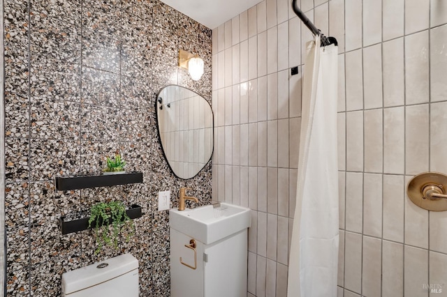 full bath featuring tiled shower, a sink, tile walls, and toilet