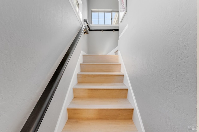 stairs with wood finished floors and a textured wall