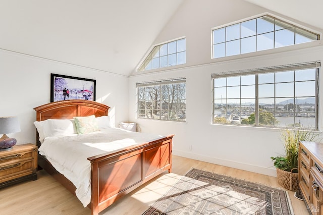 bedroom with light wood-style floors, baseboards, multiple windows, and high vaulted ceiling