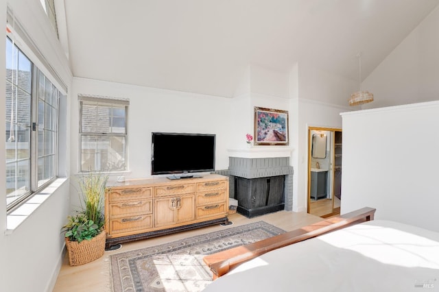 bedroom with high vaulted ceiling, a brick fireplace, multiple windows, and light wood-style flooring